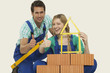 Foto: man and woman behind stack of bricks holding tape measure and spirit level, portrait man and woman behind stack of bricks holding tape measure and spirit level, portrait