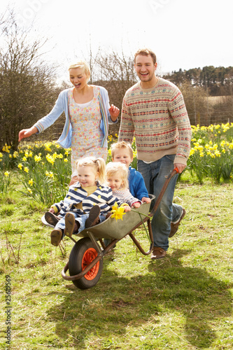 Foto: Father Giving Children Ride In Wheelbarrow Through Field Of Spri Father Giving Children Ride In Wheelbarrow Through Field Of Spri