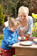 Mother And Son Decorating Easter Eggs On Table Outdoors
