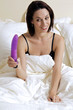 Young woman holding dildo on bed, smiling
