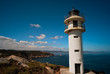 A lighthouse over the rocks agaist a blue sky with some clouds