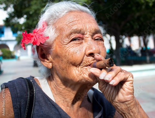 Photo: Old wrinkled woman with red flower smoking cigar. Cuba Old wrinkled woman with red flower smoking cigar. Cuba