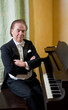 Senior man pianist is sitting next to a grand piano