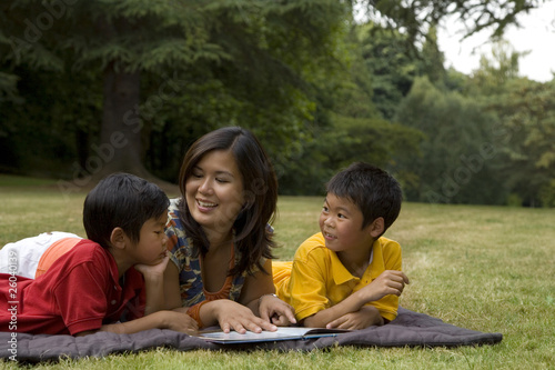 Photo: Asian mother reading book to sons in park Asian mother reading book to sons in park
