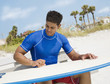Hispanic man waxing surfboard at beach