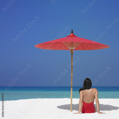Foto: Woman sitting under umbrella at beach Woman sitting under umbrella at beach