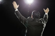 Hispanic man standing with arms raised under spotlight