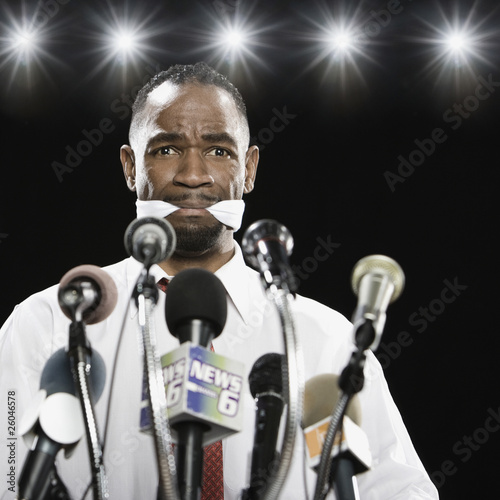 Photo: African American man at press conference podium with gag in mouth African American man at press conference podium with gag in mouth