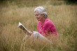A senior woman sitting on the grass, reading a book