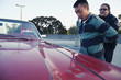 Policewoman handcuffing man against convertible