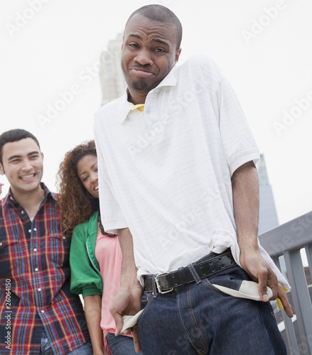 Photo: African man showing empty pockets with friends in background African man showing empty pockets with friends in background