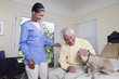 Home nurse and elderly man petting dog on bed