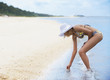 Mixed race woman in bikini picking up seashell on beach