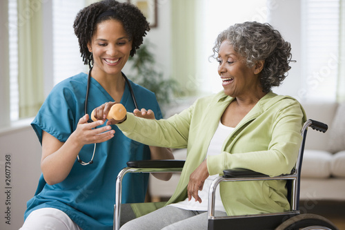 Photo: African home nurse helping woman in wheelchair with hand weight African home nurse helping woman in wheelchair with hand weight
