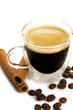 espresso in einer glastasse daneben kaffeebohnen und zimtstangen