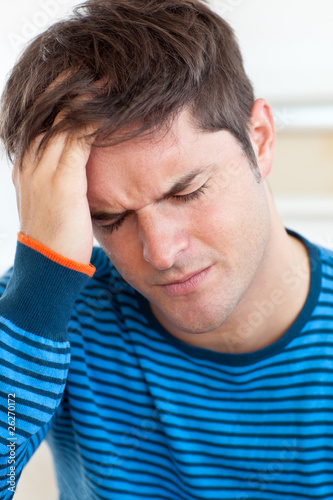 Photo: Cute man having a headache in the living-room Cute man having a headache in the living-room