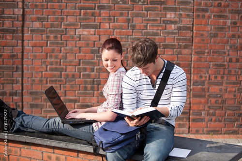 Photo: Two students working together with book and laptop outside Two students working together with book and laptop outside