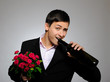 Handsome romantic young man holding rose flower and vine bottle