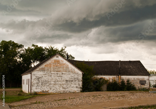 Photo: An old white buiding in front of a dark, dramatic prairie sky An old white buiding in front of a dark, dramatic prairie sky