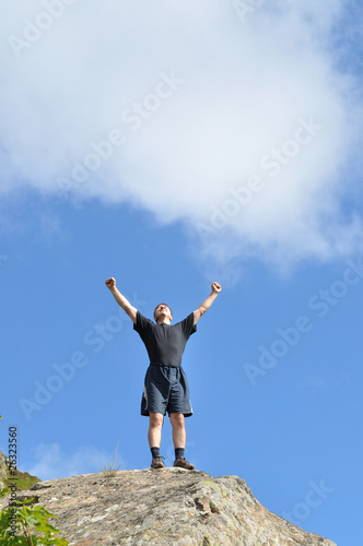 Photo: A young man stands on a cliff top and raised his hands A young man stands on a cliff top and raised his hands
