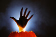 Human hand raising from glowing pumpkin Jack-o-lantern