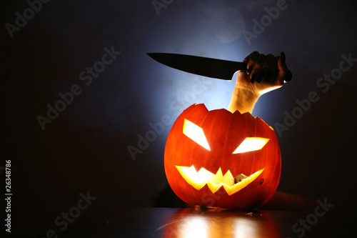 Photo: Hand with knife raising from glowing pumpkin lantern Hand with knife raising from glowing pumpkin lantern