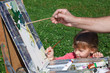 Easel artist in nature. Girl learns to paint with adult.
