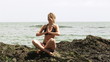 Video: Young woman doing yoga sitting on rocks with ocean on background Young woman doing yoga sitting on rocks with ocean on background
