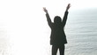 Rear view of a woman raising her arms in front of the ocean