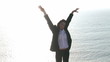Woman raising her arms standing on the edge of a cliff