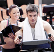 Smart female coach taking notes while her pupil is pedaling