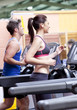 Pretty woman with earphones using a treadmill with her boyfriend