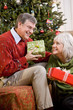 Photo: Senior couple exchanging gifts by Christmas tree Senior couple exchanging gifts by Christmas tree
