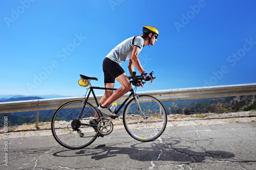 Photo : Cyclist riding a bike uphill along a road; clear summer day Cyclist riding a bike uphill along a road; clear summer day
