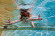 The girl smiles, swimming under water in the pool