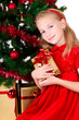 Photo: Young girl with gift sit near Christmas tree. Young girl with gift sit near Christmas tree.