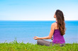 Beautiful young woman meditating with a view of the ocean