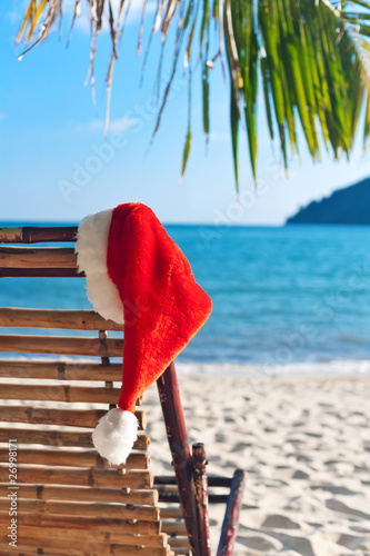 Photo: Red Santa's hat hanging on beach chair under palm tree Red Santa's hat hanging on beach chair under palm tree