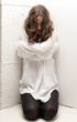 Young insane woman with straitjacket on knees looking at camera