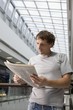 Young man stands reading newspaper in new shopping centre, Voronezh