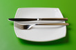 White square plate, knife, and fork on green background