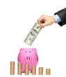 Man inserting a dollar into a piggy bank with stack of coins in Man inserting a dollar into a piggy bank with stack of coins in