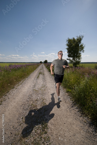 Foto: Athletic male running on field road on hot summer day. Athletic male running on field road on hot summer day.
