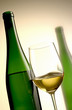 glass of white wine with green bottle in the background