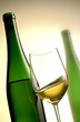 glass of white wine with green bottle in the background