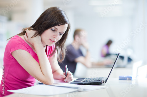 Photo: in the library - pretty female student with laptop and books wor in the library - pretty female student with laptop and books wor
