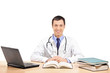 A doctor posing in his office, with laptop and many book
