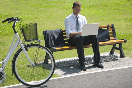 Photo: Businessman sitting on bench with laptop and bicycle Businessman sitting on bench with laptop and bicycle