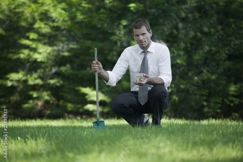 Photo: Businessman on lawn with shovel and jar of coins Businessman on lawn with shovel and jar of coins