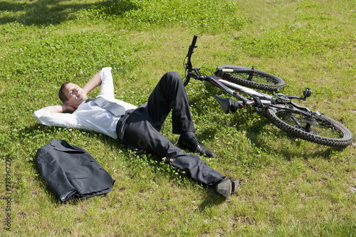 Photo: Businessman lying down in grass next to bicycle enjoying the sun Businessman lying down in grass next to bicycle enjoying the sun
